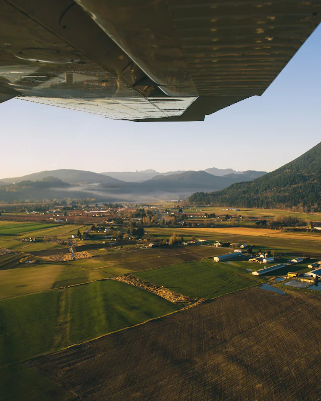 Farmland and hills seen from a small aircraft cabin, with the wing and strut in view