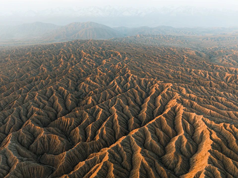 Aerial view of eroded badland ridges running to distant mountains, Kyrgyzstan