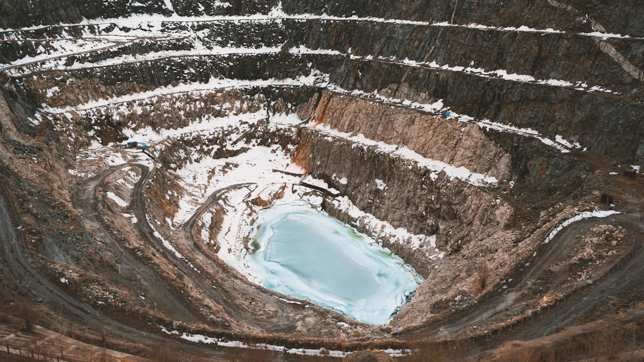 Aerial view of a deep terraced open-pit mine with a pit lake, Altay, China